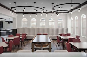 Un comedor moderno con una mesa larga rodeada de sillas rojas, un sofá y una cocina al fondo.