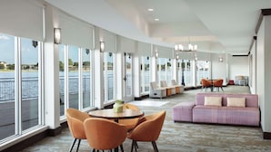 A spacious room with large windows overlooking a body of water, a round table with chairs, a sofa, and a small table with a plant. - Hilton Garden Inn Granbury (Granbury)