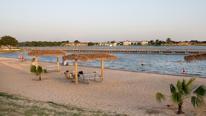 A beach with thatched-roof structures, a pier, and a calm sea. - Hilton Garden Inn Granbury (Granbury)