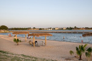 Una playa con estructuras de techo de paja, un muelle y un mar tranquilo.