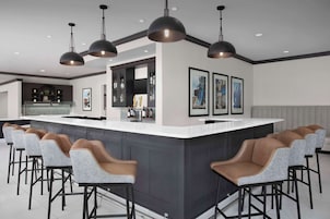 Una cocina moderna con una isla central, taburetes de bar, iluminación colgante y cuadros en las paredes.