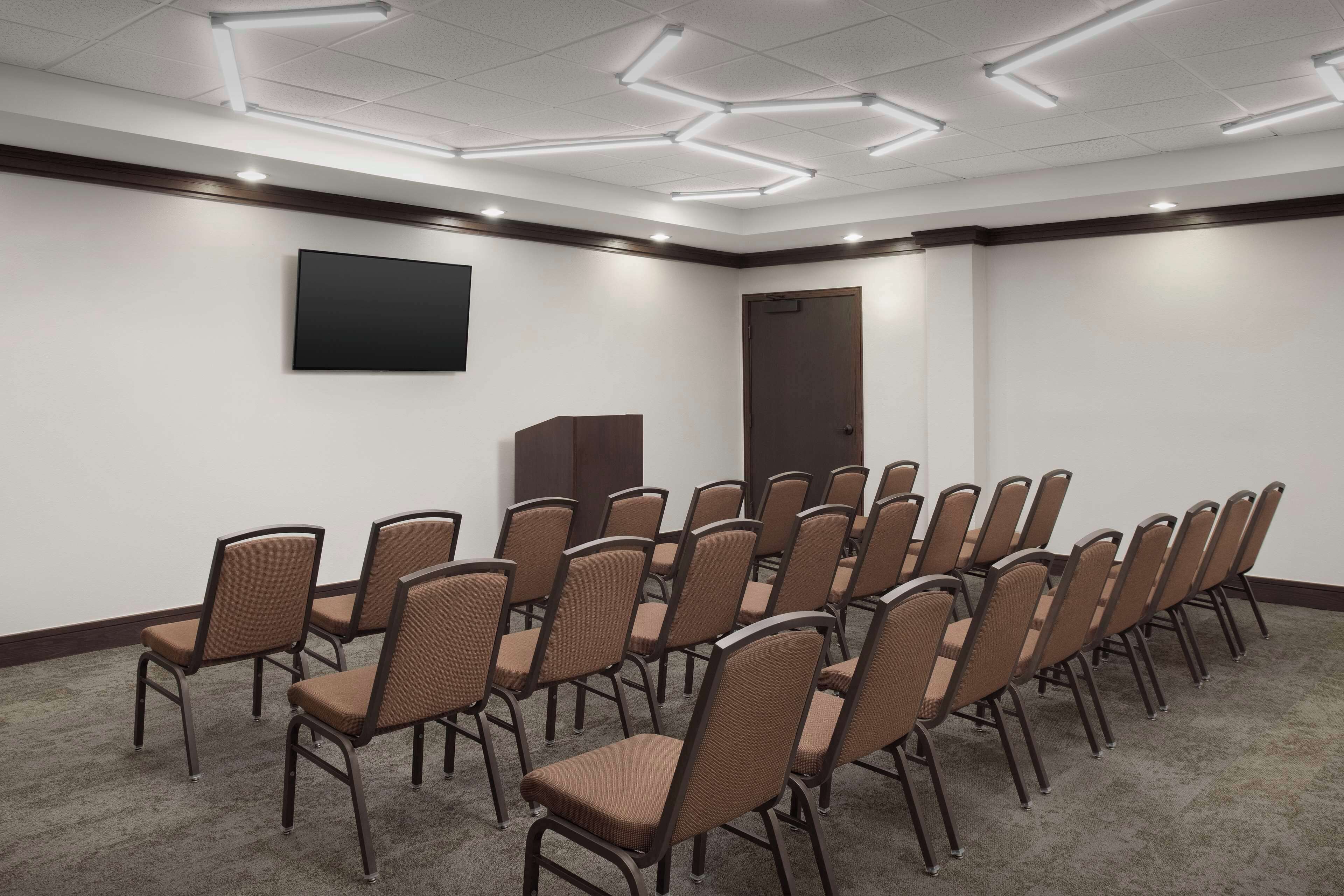 A conference room with rows of chairs, a flat-screen TV, and a door.