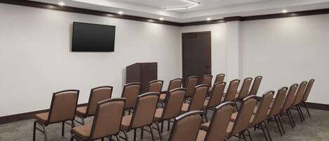 A conference room with rows of chairs, a flat-screen TV, and a door.