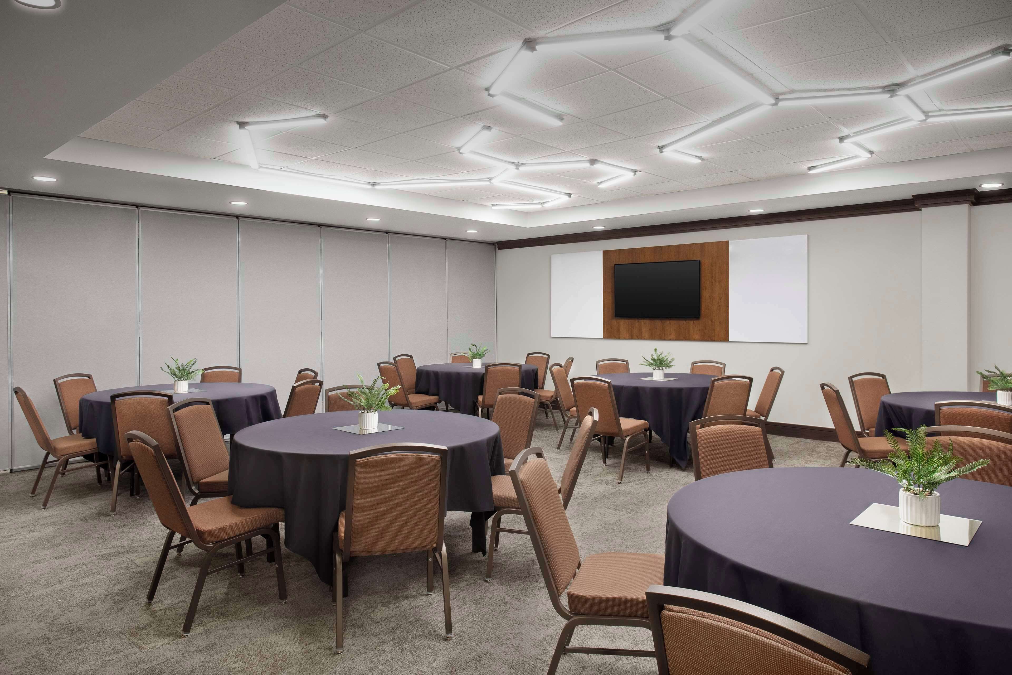 A conference room with round tables, chairs, and a large screen on the wall.