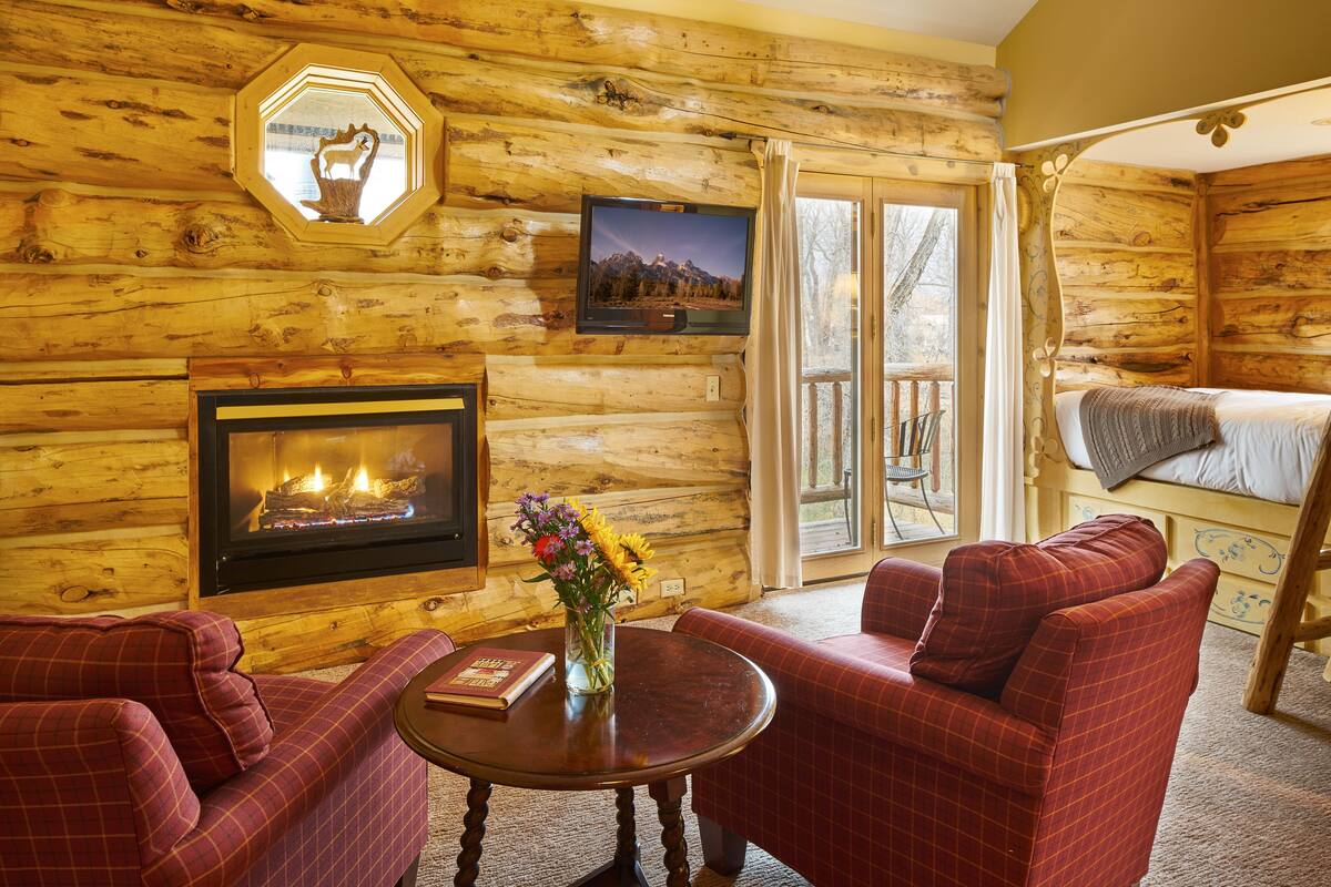 A log cabin interior with a fireplace, a television, a dining table, and a cozy seating area.