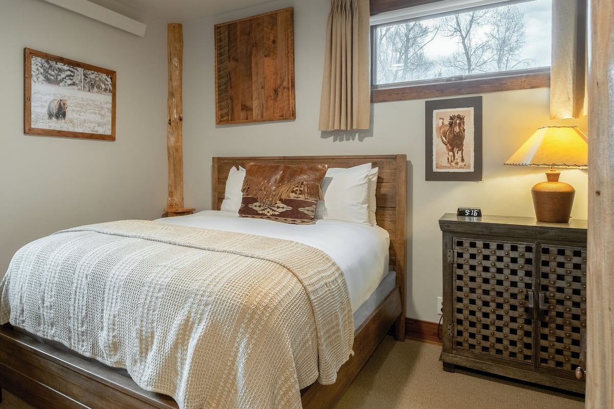 A bedroom with a bed, a wooden headboard, a nightstand, a lamp, and a picture of a horse on the wall.