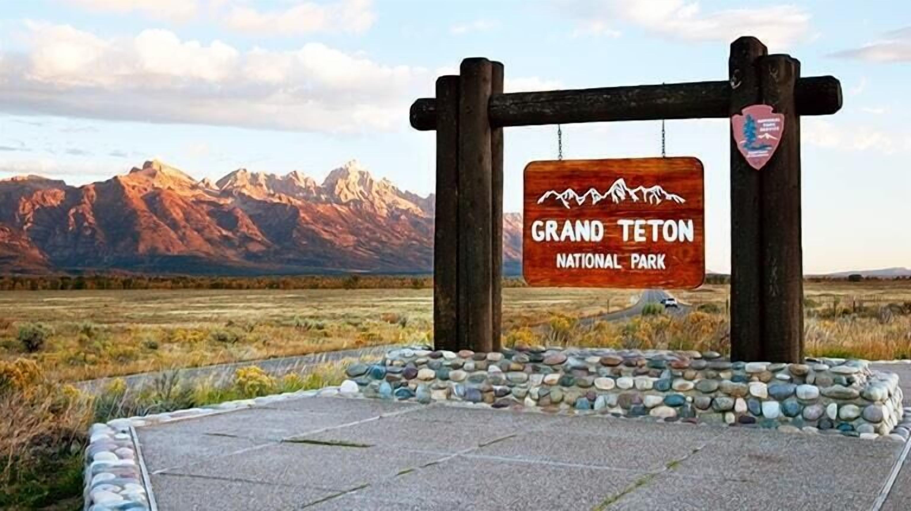 A wooden sign for Grand Teton National Park with a mountainous backdrop.