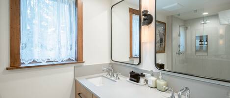 A bathroom with a double sink, a large mirror, and a window with lace curtains.
