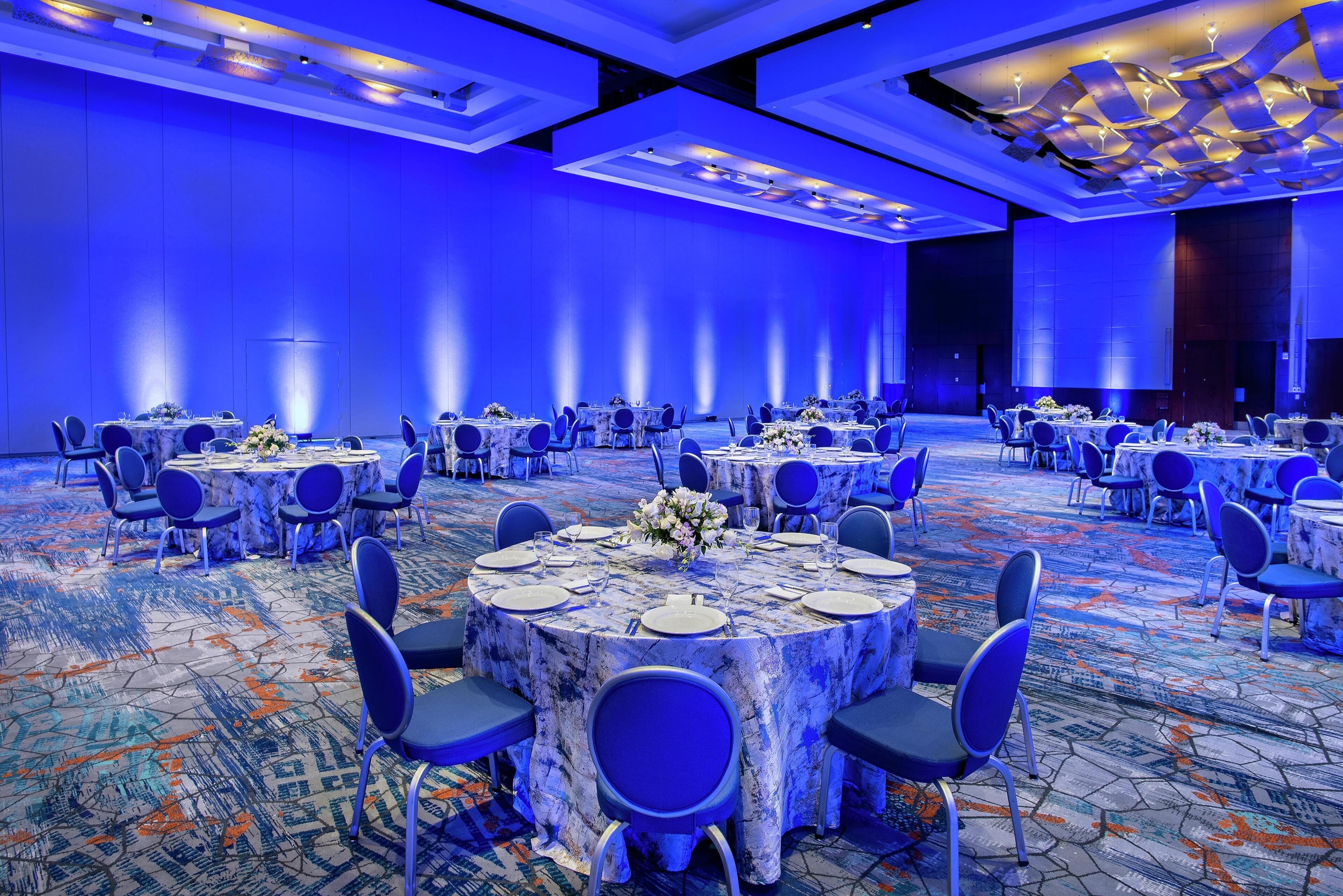A large conference room with round tables, blue chairs, and a patterned carpet.