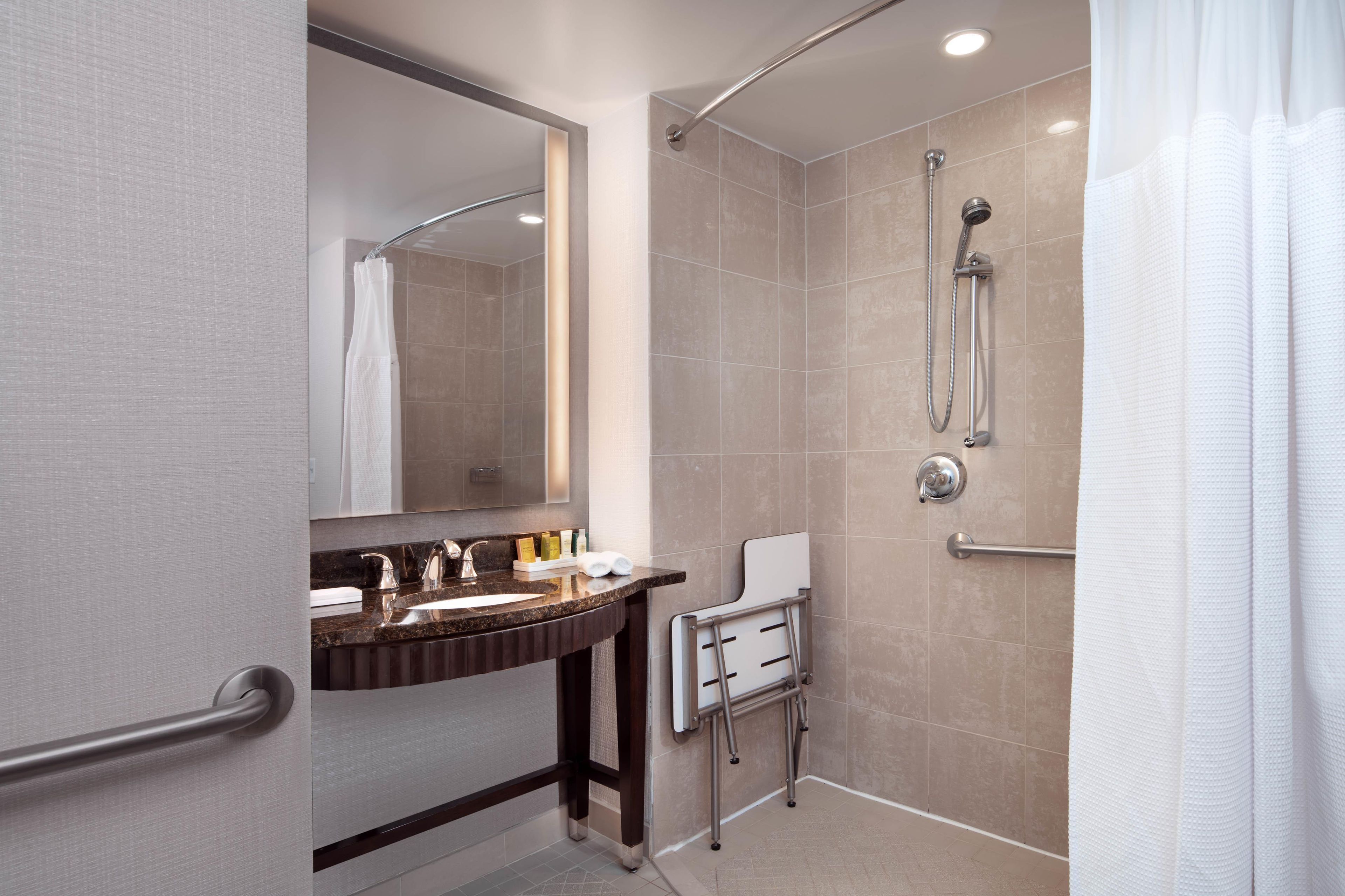 A modern bathroom with a vanity, mirror, shower, and handrails.