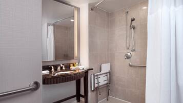 A modern bathroom with a vanity, mirror, shower, and handrails.