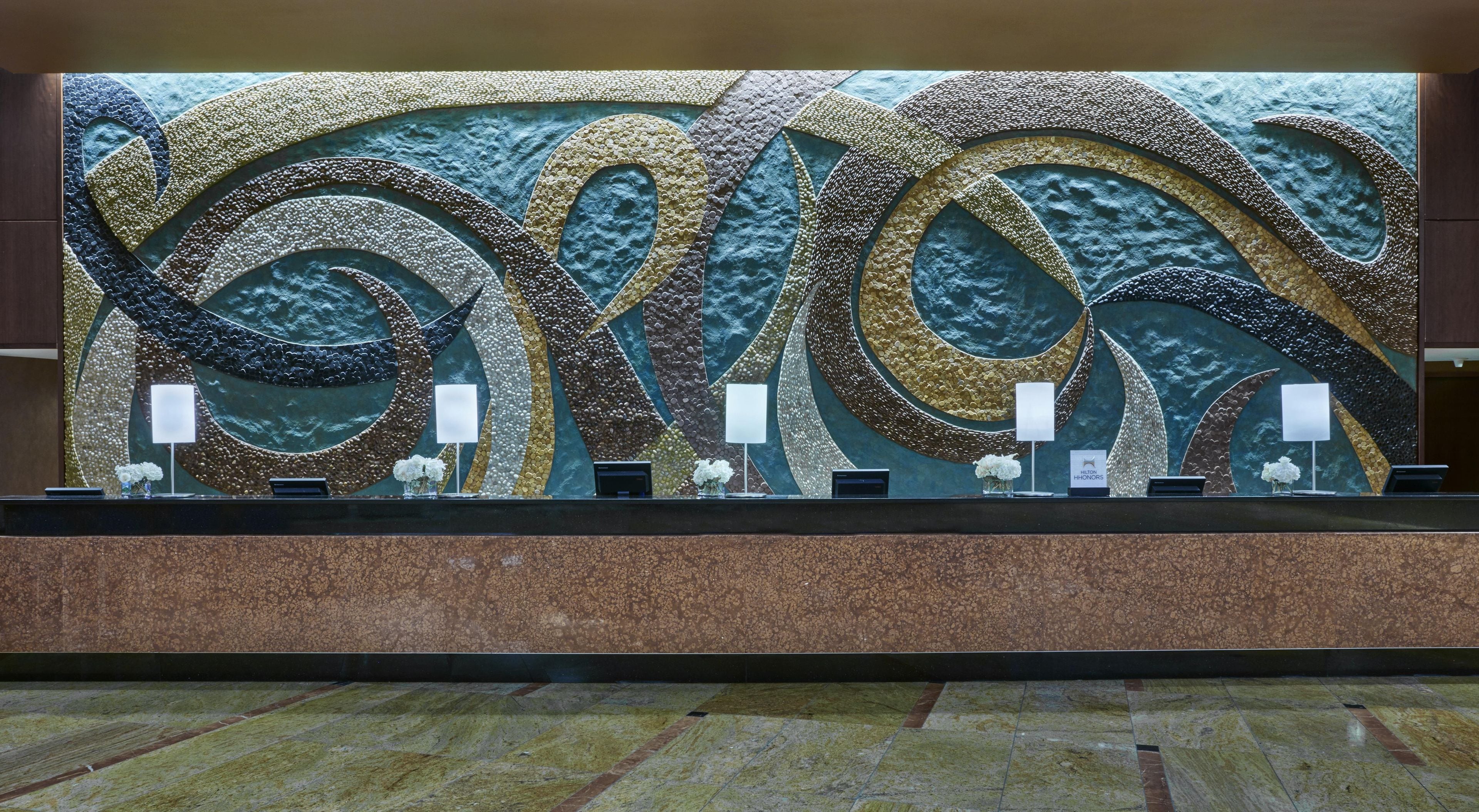 A reception desk with a decorative wall mural, a marble floor, and a sign indicating the hotel name.