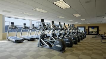 A gym with treadmills, elliptical machines, and stationary bikes arranged in rows.
