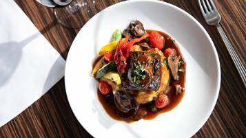 Ein Teller mit Essen, darunter verschiedene Gemüsesorten und Fleisch, dazu ein Glas Rotwein und eine Gabel auf einem Holztisch.