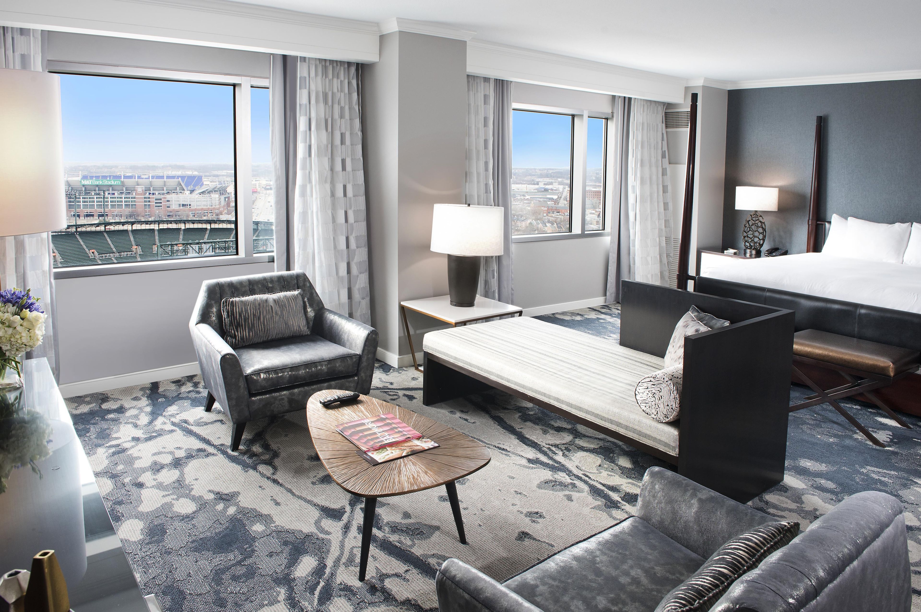 Une chambre d ’hôtel avec un lit, un canapé, une chaise, une table basse et une vue sur un stade.