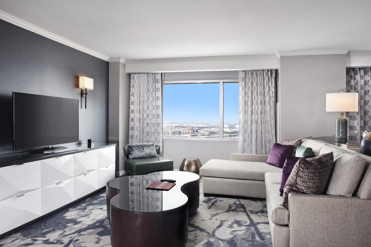 A modern hotel room with a flat-screen TV, a sofa, a coffee table, and a view of the city.