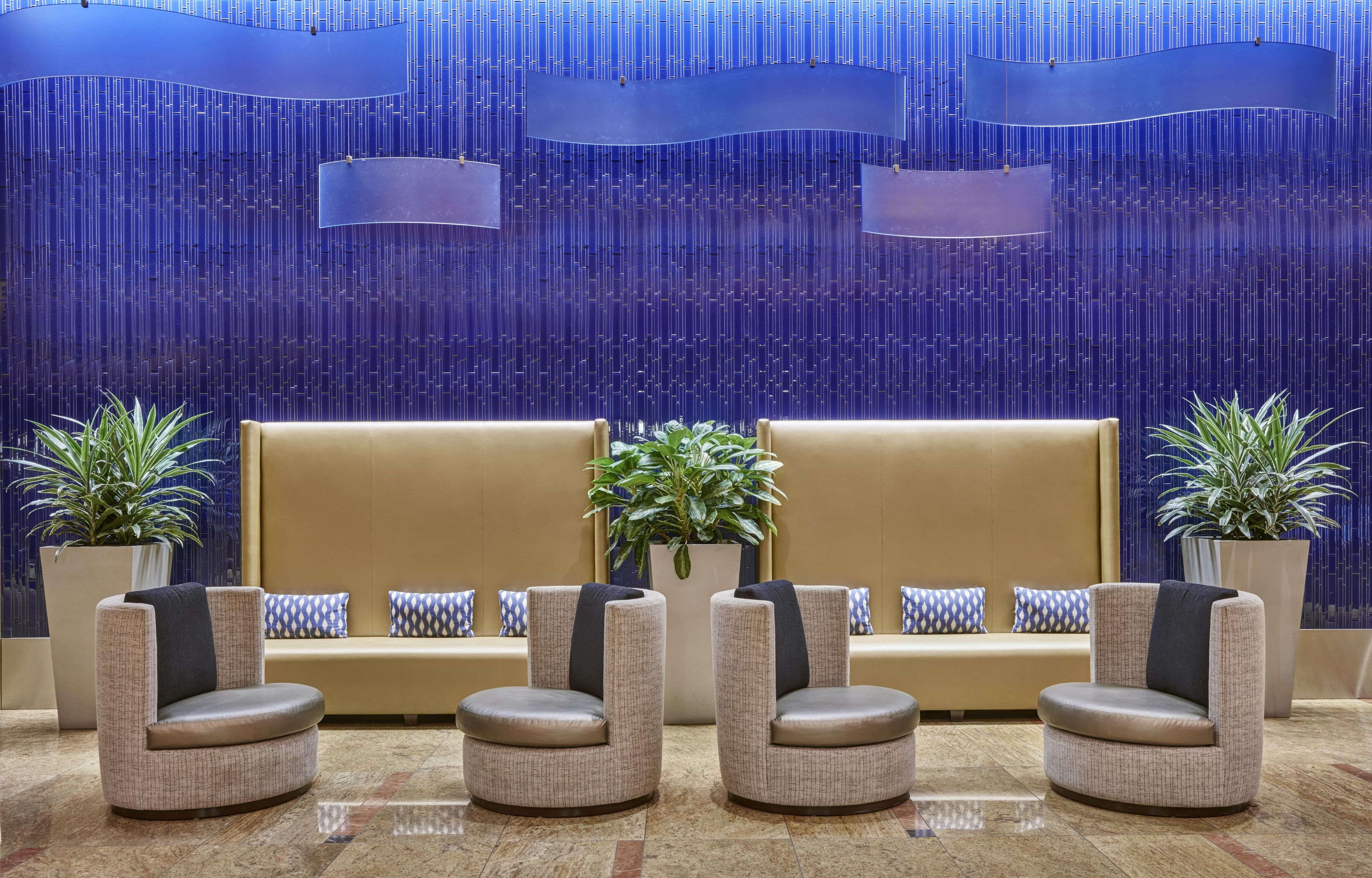 A lobby with a sofa and armchairs, potted plants, and a patterned wall.