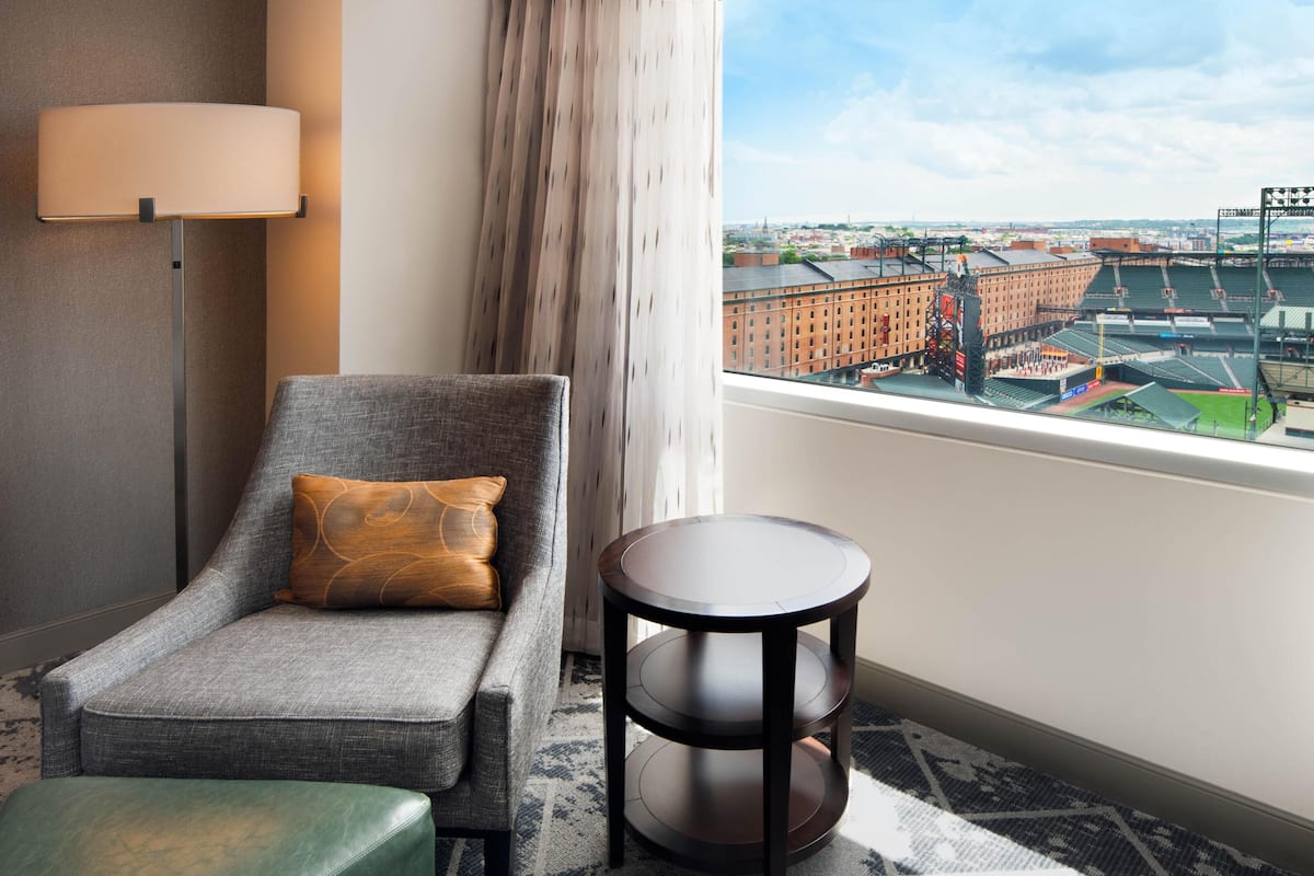 A hotel room with a view of a stadium, a sofa, a small table, and a lamp.