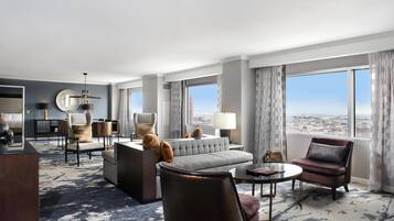 A modern hotel room with a large bed, a sofa, a dining area, and a view of the city.