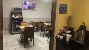 A breakfast area with tables and chairs, a microwave, and a television displaying a show.