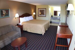 A hotel room with a large bed, a sofa, a small table, a desk, a mirror, and a bathroom with a sink and toilet. - Loyalty Inn Hawkinsville (Hawkinsville)