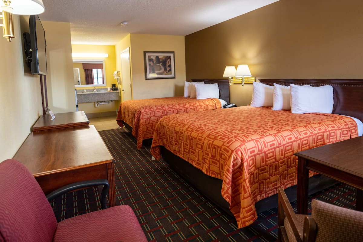 A hotel room with two beds, a desk, a chair, a lamp, and a painting on the wall.