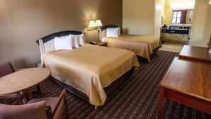 A hotel room with two beds, a desk, a chair, and a small table.