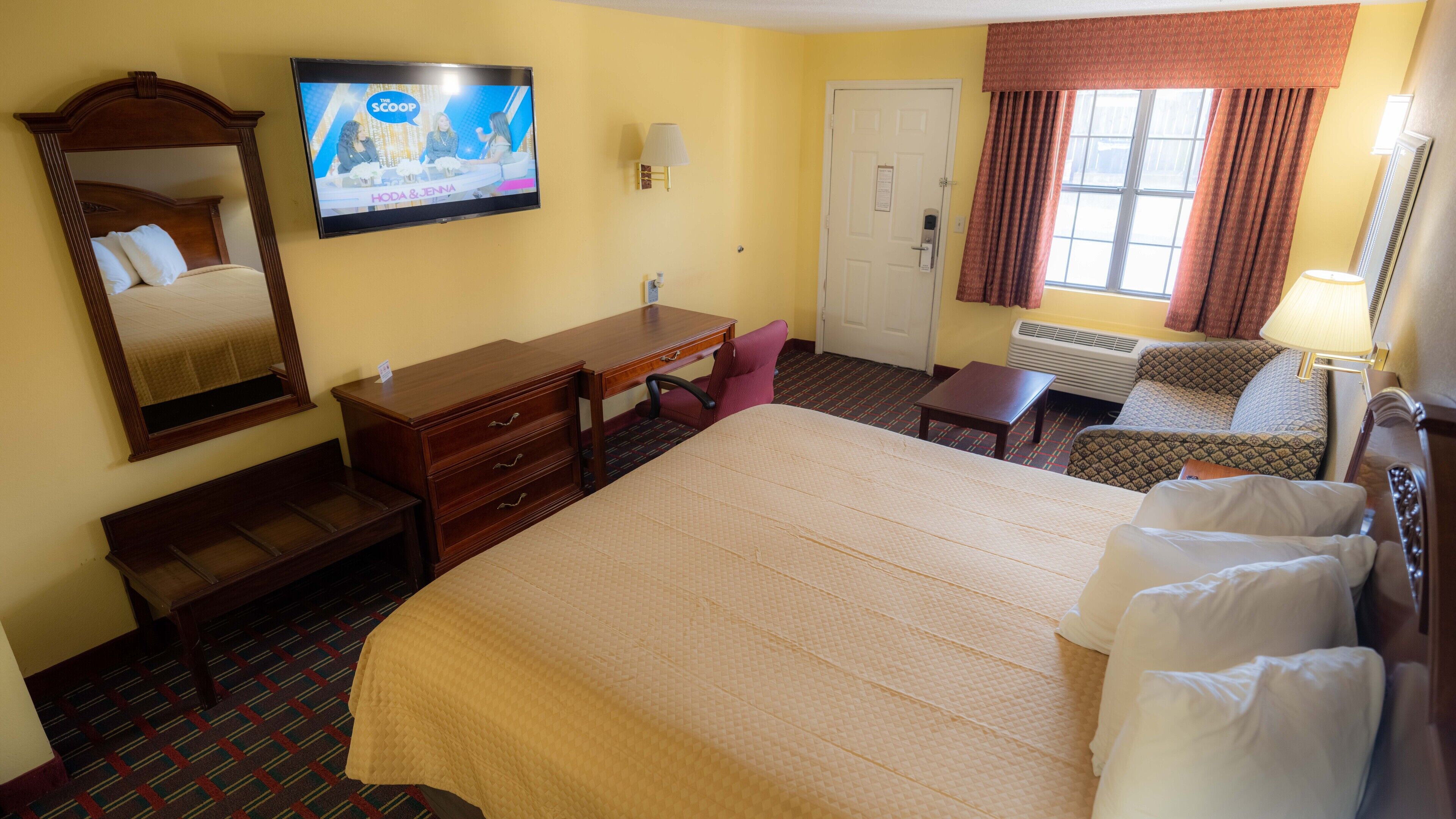 Une chambre d’hôtel avec un grand lit, un bureau, une chaise, une télévision et une fenêtre avec des rideaux.