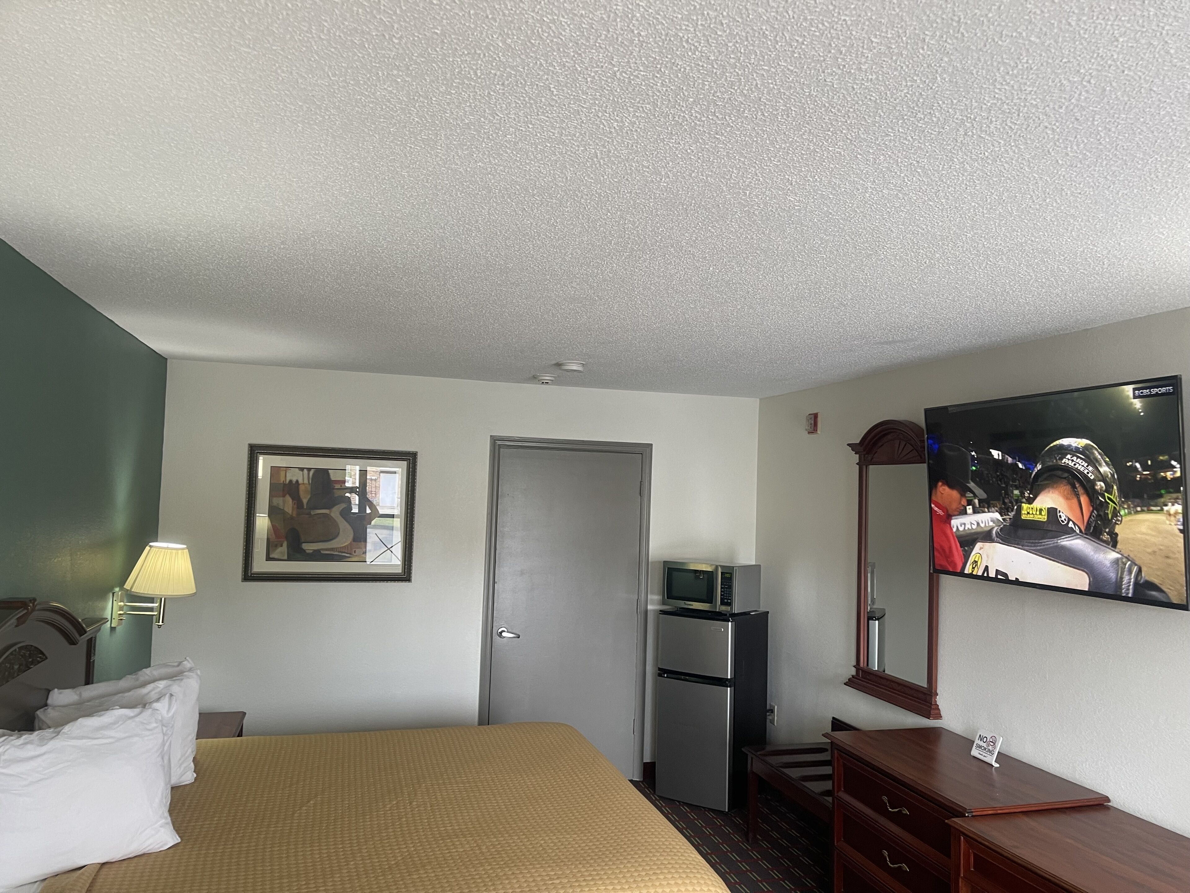 A hotel room with a bed, a desk, a television, a refrigerator, and a door.