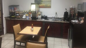 A small kitchen with a dining table and chairs, a microwave, a coffee maker, and various kitchen appliances. - Loyalty Inn Hawkinsville (Hawkinsville)