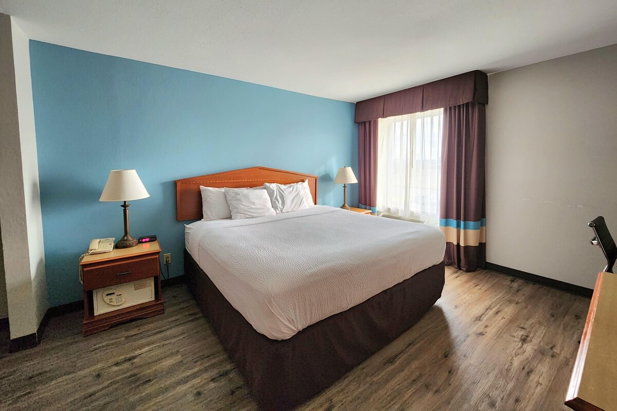 Habitació d'hotel amb un llit gran, dues taules de nit amb làmpades, una meseta amb un telèfon i una finestra amb cortines.