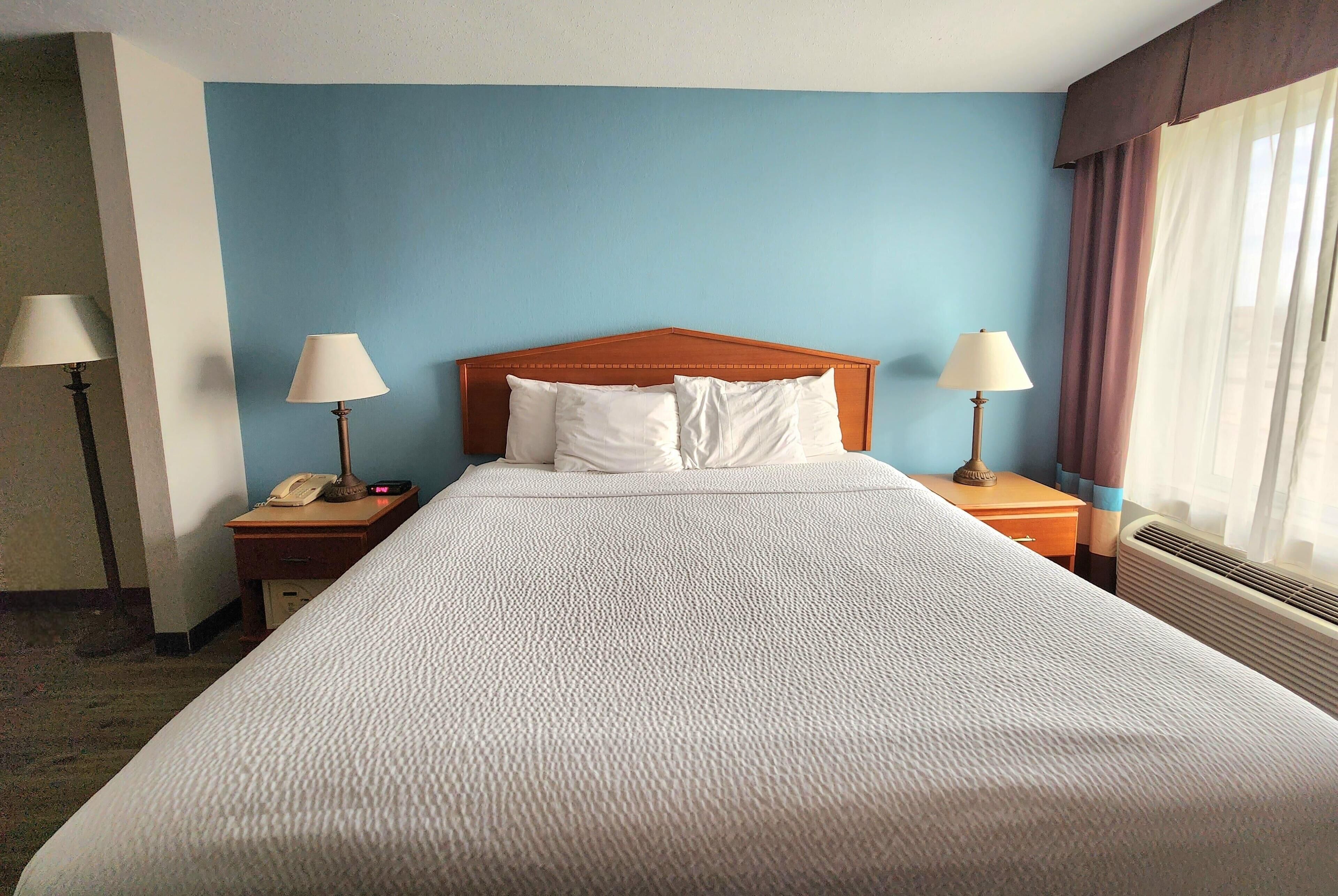 A hotel room with a large bed, two bedside tables with lamps, a telephone, and a window with curtains.