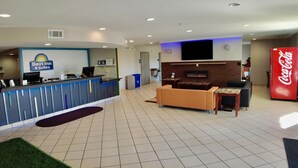 A reception area with a Days Inn & Suites sign, a flat-screen TV, a Coca-Cola refrigerator, and a seating area with a fireplace.