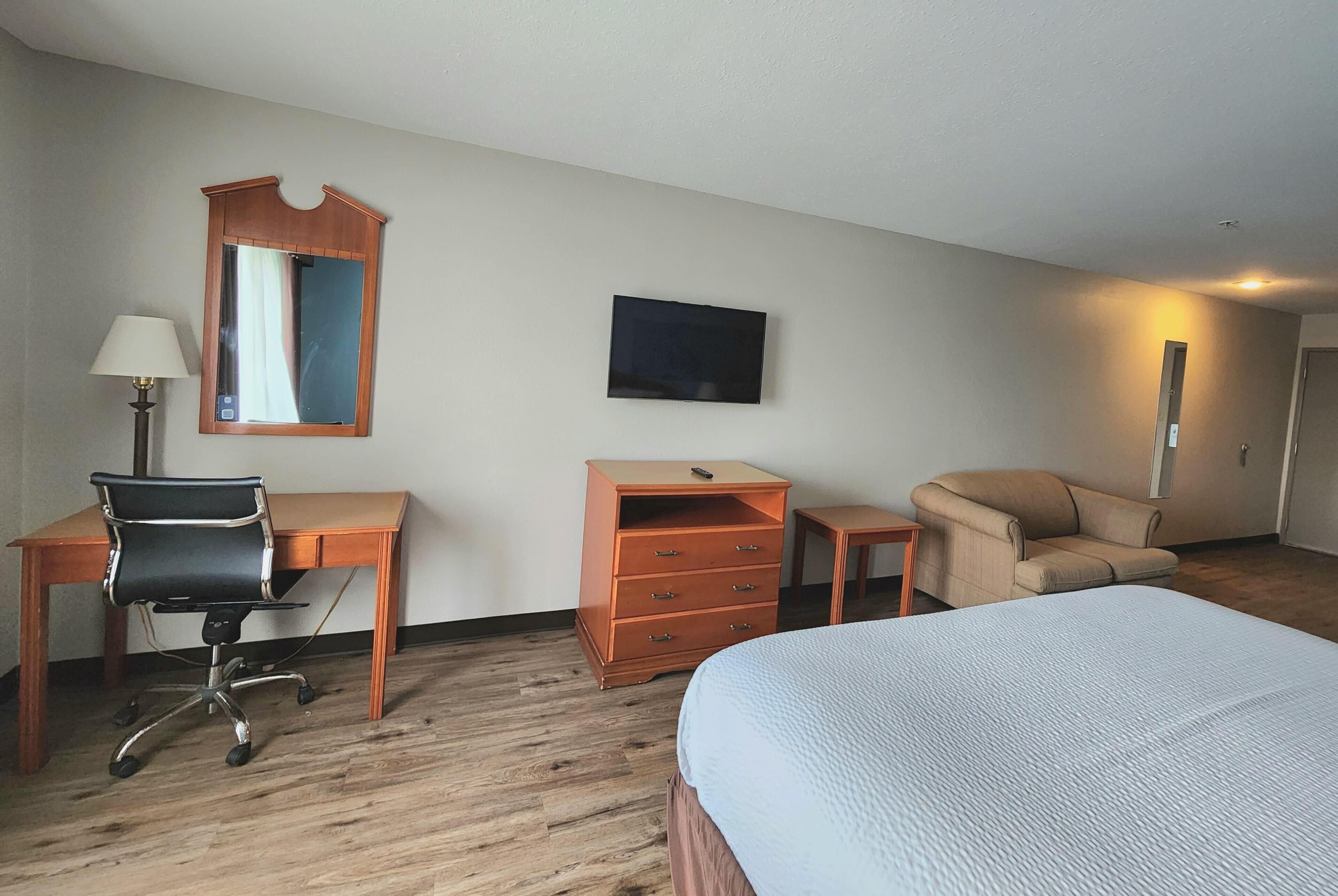 A hotel room with a bed, desk, chair, dresser, and a TV on the wall.