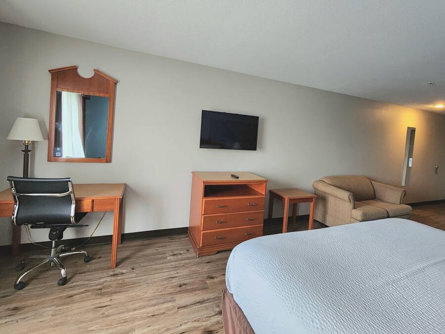 A hotel room with a bed, desk, chair, dresser, and a TV on the wall.