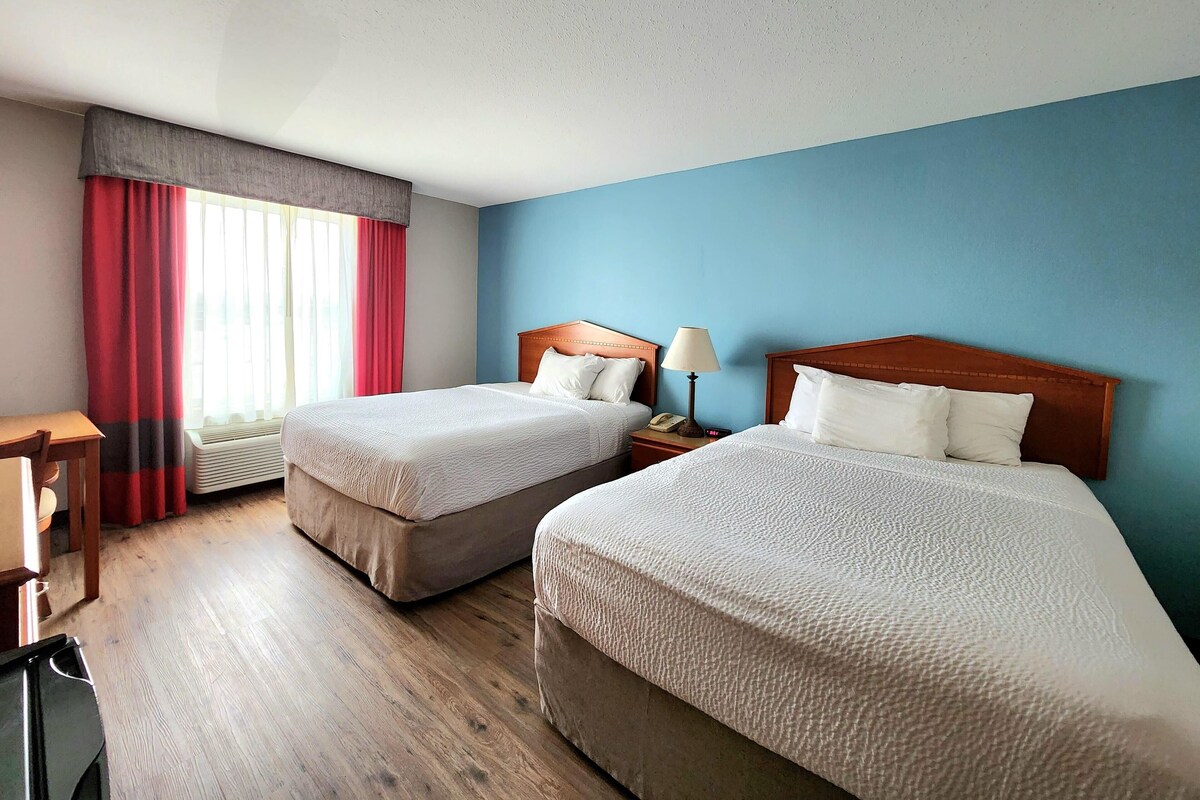 Habitació d'hotel amb dos llits, un escriptori i una finestra amb cortines.