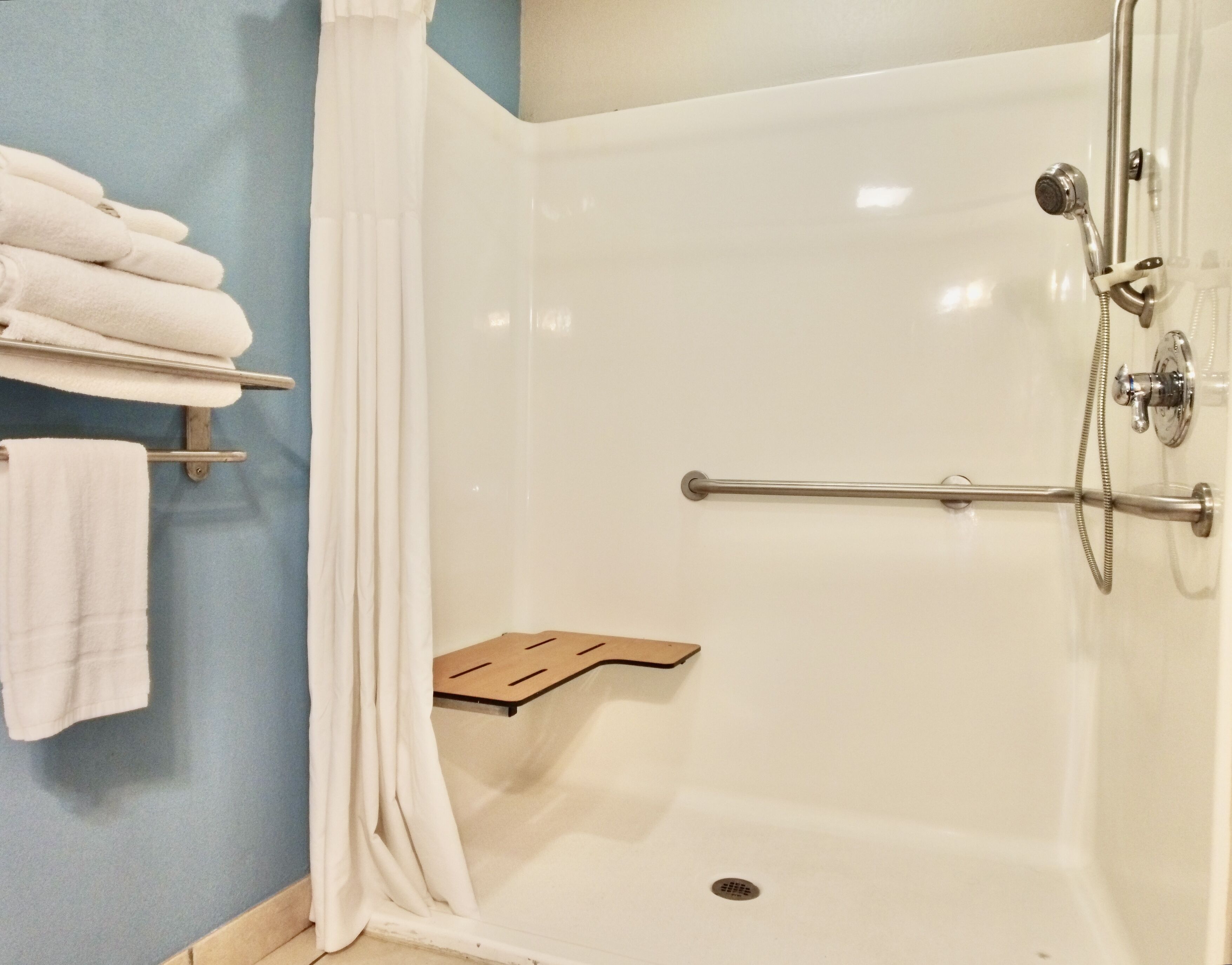 A shower with a grab bar, a towel rack with folded towels, and a shower seat.