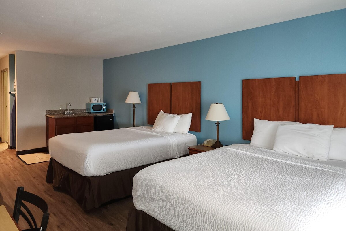 Habitació d'hotel amb dos llits, una taula de nit amb microones i una cadira.