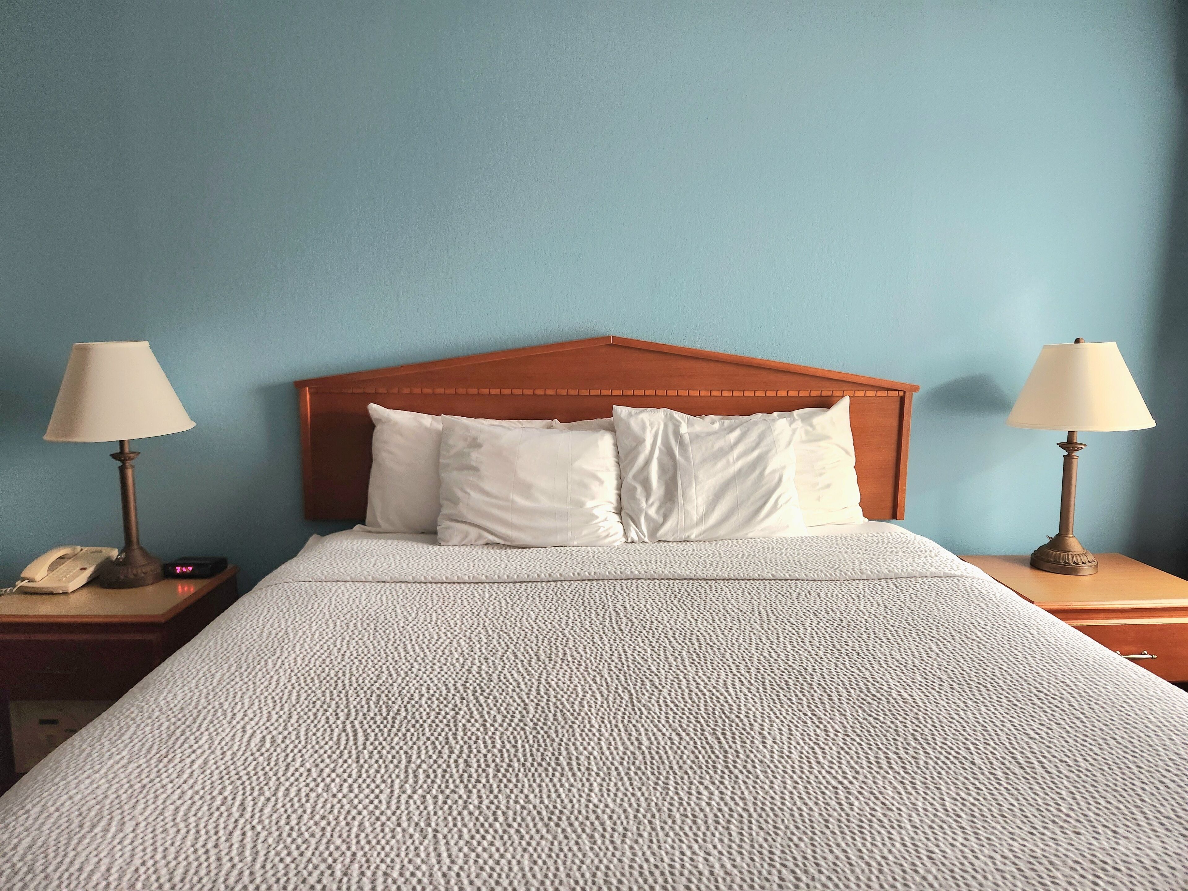 Habitación de hotel con cabecera de madera, dos mesitas de noche con lámparas, cama con ropa blanca y pared azul.