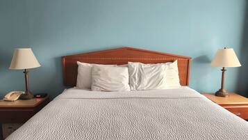 Habitación de hotel con cabecera de madera, dos mesitas de noche con lámparas, cama con ropa blanca y pared azul.