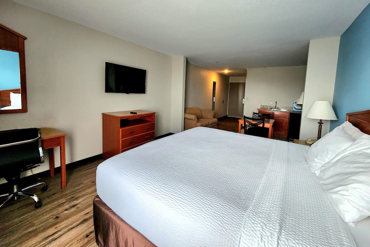 A hotel room with a large bed, a desk, a chair, a television, and a desk lamp.