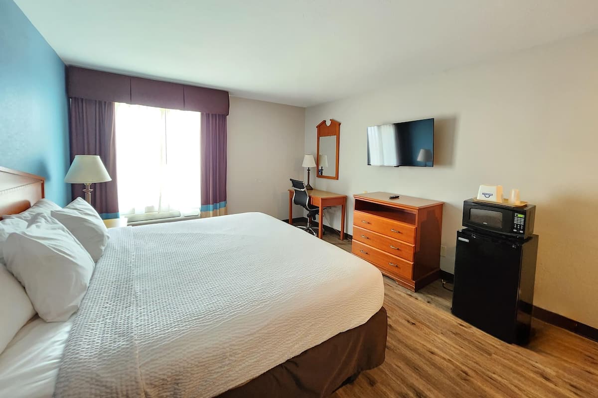 A hotel room with a bed, desk, chair, dresser, television, and a microwave.
