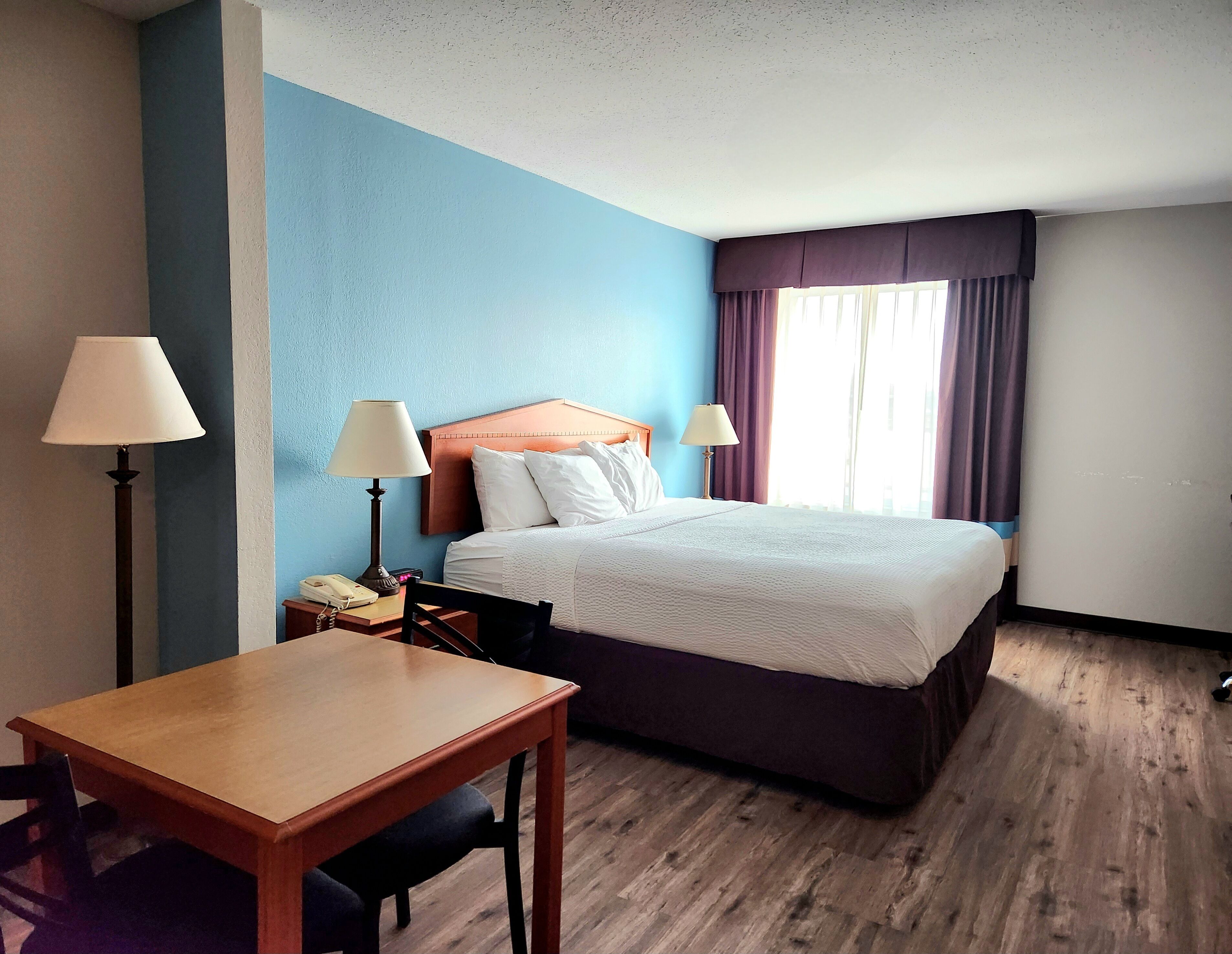 A hotel room with a bed, two bedside lamps, a wooden desk, and a chair.