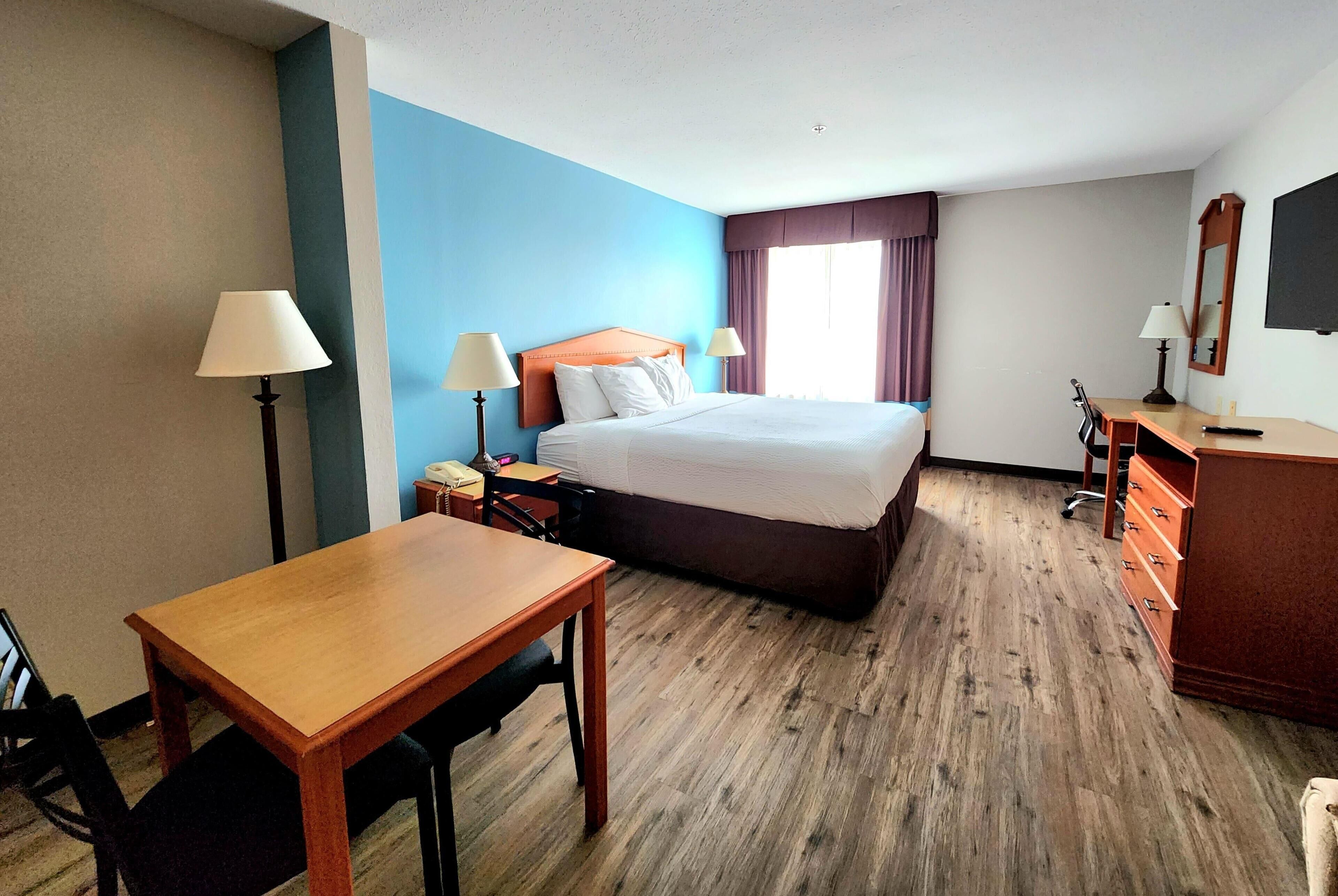 A hotel room with a bed, a desk, a chair, a dresser, and a TV.