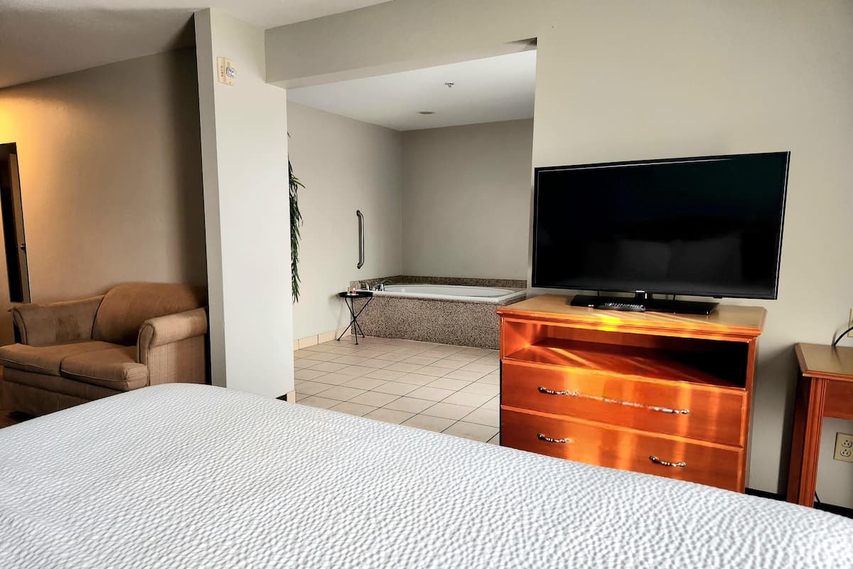A hotel room with a bed, a TV on a wooden dresser, a sofa, and a bathroom with a bathtub.