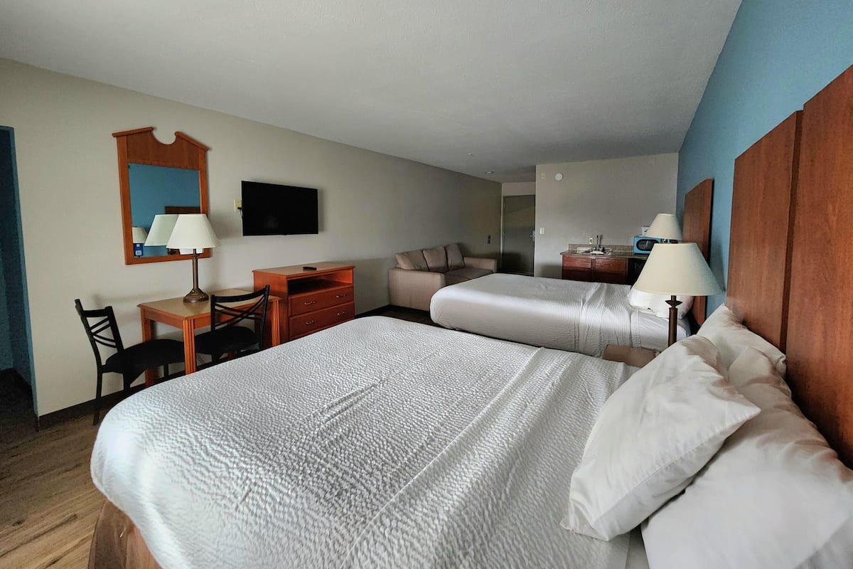 A hotel room with two beds, a desk, a chair, a TV, and a mirror.