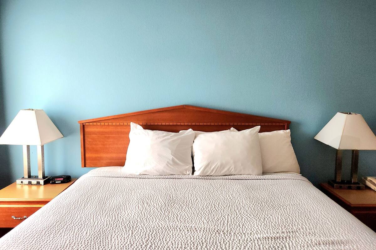 A neatly made bed with a wooden headboard, two bedside tables with lamps, and a blue wall.