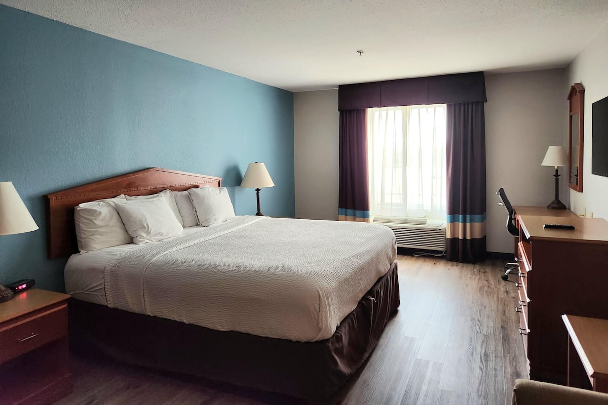 A hotel room with a large bed, two bedside tables with lamps, a desk with a chair, and a window with curtains.