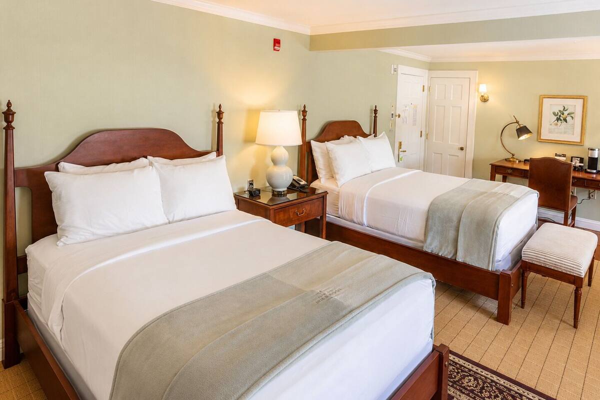 Une chambre d’hôtel avec deux lits, un bureau, une chaise, une lampe et un tableau encadré au mur.
