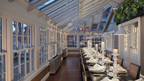 A long dining table set with white tableware, flanked by windows and a skylight. - Inn on Boltwood (Amherst)